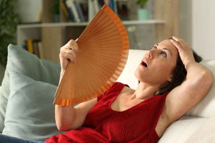 donna che soffre il caldo sul divano con ventaglio in mano 