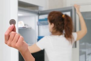 donna che apre freezer e mano che tiene una monetina